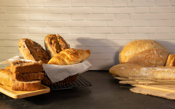 Assortment of freshly baked bread on wooden table against brick wall. - Zdjęcie, obraz