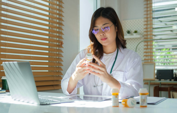 Женщина-врач держит бутылку с таблетками, работает с медицинскими документами в медицинском кабинете. Медицинское обслуживание, концепция аптеки.  - Фото, изображение