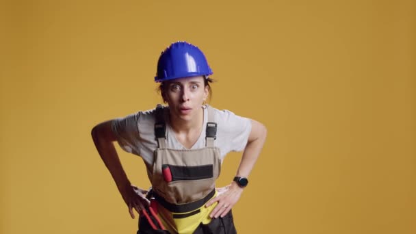 Porträt einer selbstbewussten Heimwerkerin, die neugierig und forschend über gelbem Hintergrund steht. Bauunternehmerin schaut in Kamera und albert herum, untersucht und sucht Überraschung. - Filmmaterial, Video