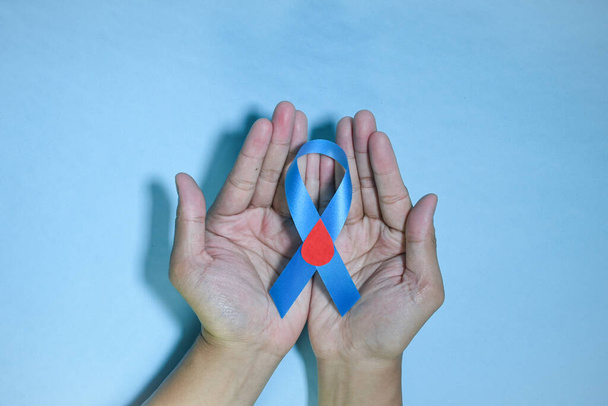 Blaues Band mit rotem Blutstropfen in den Händen isoliert auf blauem Hintergrund. 14. November, Weltdiabetestag. Kopierraum - Foto, Bild