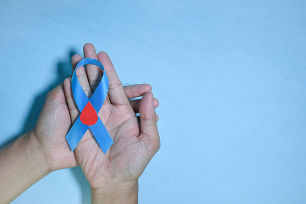 Top View Blue ribbon awareness with red blood drop in man hands isolated on a blue background. 14 november, World diabetes day. Copyspace - Photo, image