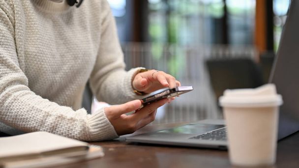 фотография крупным планом и боковым видом, молодая женщина в удобном свитере с мобильного телефона, работающая в кофейне. - Фото, изображение