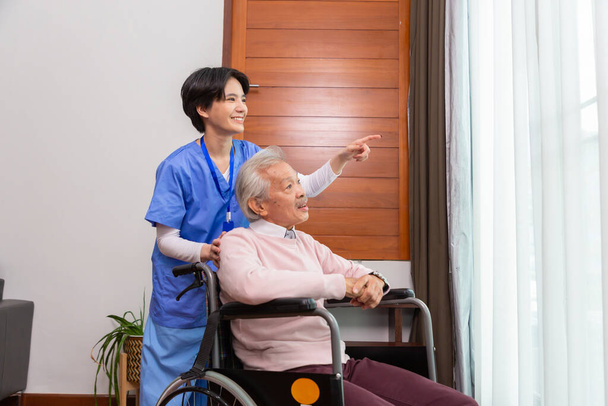 Barátságos személyzet gondozó idősek otthona beszél ázsiai idősebb férfi a nappaliban. - Fotó, kép