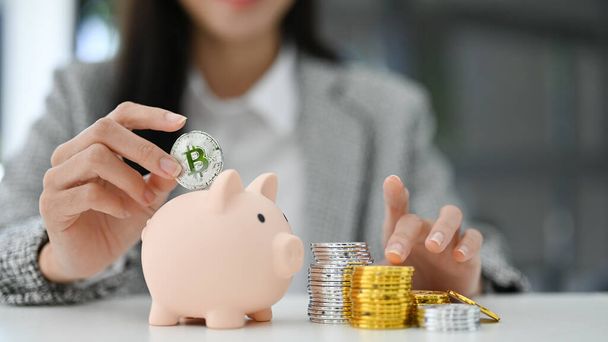 Beautiful Asian businesswoman insert coins in a pin piggy bank on the table. saving money, investment, currency concept. cropped and close-up image - Photo, Image