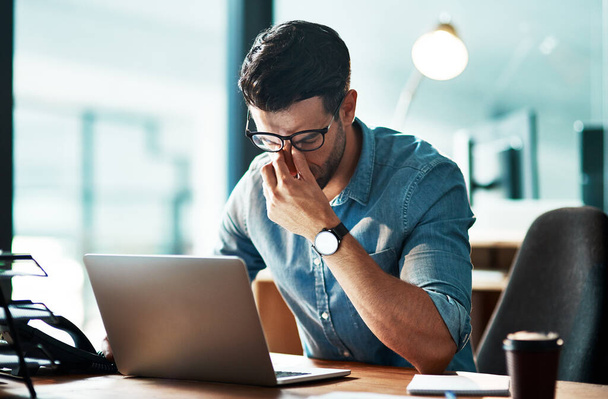 A csiszolás kikészíti. egy fiatal üzletember tapasztalt stressz használata közben egy laptop egy modern irodában - Fotó, kép