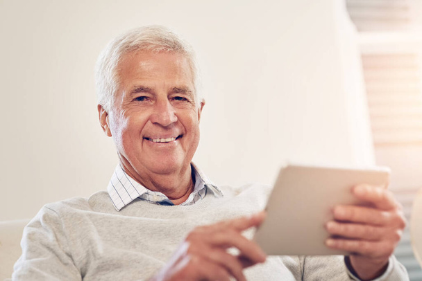 Ich beschäftige mich gerne. Porträt eines älteren Mannes, der zu Hause ein digitales Tablet benutzt - Foto, Bild