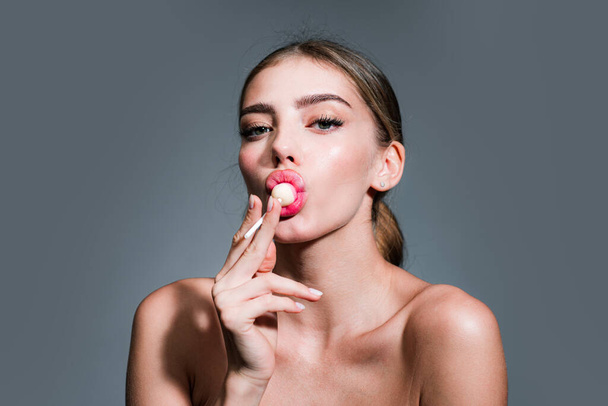 Sexy woman face. Beautiful amazing sexy woman iwith a lollipop on studio background. Fashion model portrait licking candy - Fotó, kép