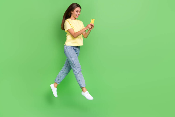 Full length photo of positive cute lady hand hold telephone run empty space use shopping online service isolated on green color background. - Photo, Image