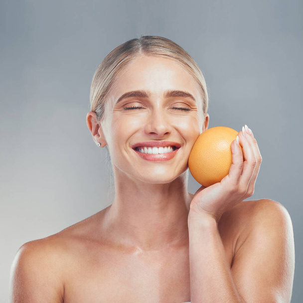 Vrouw, glimlach en oranje fruit voor huidverzorging, schoonheid en gezondheid tegen grijze studio-achtergrond voor cosmetica. Model, huid en gezicht gezondheid voor zelfverzorging, vitamine C en cosmetica voor organische dermatologie. - Foto, afbeelding