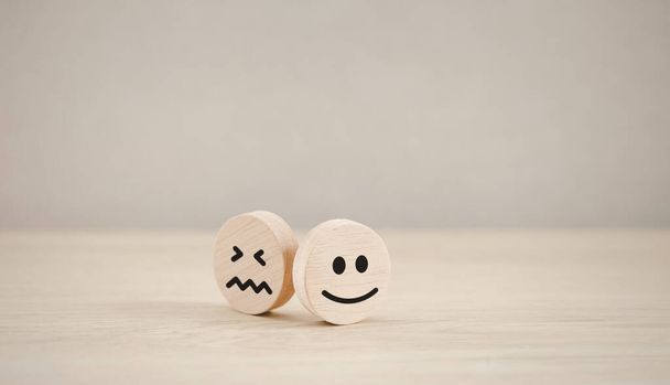 happy emotion face on wooden piece with unhappy one behind for satisfaction survey, mental health assessment - Photo, Image