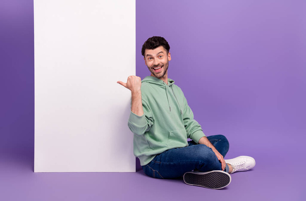 Full size photo of handsome young man sit floor point vertical menu poster wear trendy gray look isolated on violet color background. - Foto, imagen