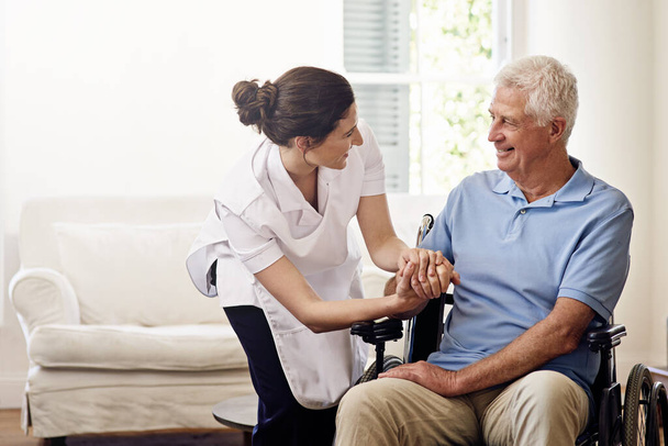 Stets mit einer helfenden Hand dabei. Eine Pflegekraft hilft einem älteren Mann im Rollstuhl zu Hause - Foto, Bild