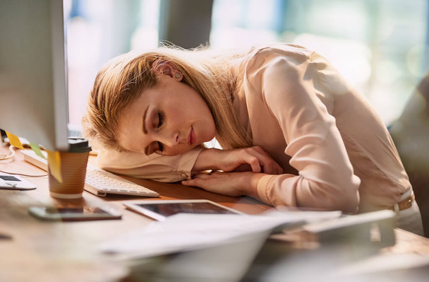 Uzun bir gün oldu. Yorgun genç bir iş kadını ofisinde masasında uyuyor. - Fotoğraf, Görsel