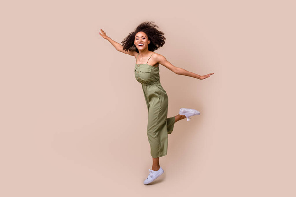 Full body photo of pretty young woman wavy hair jump spread hands plane pose dressed stylish khaki look isolated on beige color background. - 写真・画像
