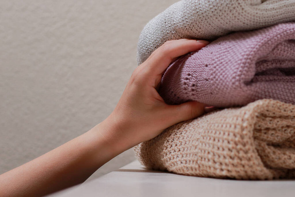 close up of female hand grabbing a sweater, stack of folded knitwear. Cozy fall and winter wardrobe. High quality photo - Zdjęcie, obraz