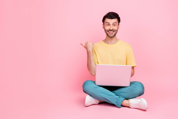 Photo of positive man wear stylish clothes sit arm direct empty space recommend fast connection wifi isolated on pink color background. - Fotografie, Obrázek