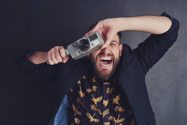 Hij is bijzonder enthousiast over filmcamera 's. een trendy jongeman met een vintage camera poserend tegen een donkere achtergrond - Foto, afbeelding