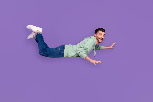 Full size photo of handsome young guy flying hovering empty space banner wear trendy gray outfit isolated on violet color background. - Foto, afbeelding