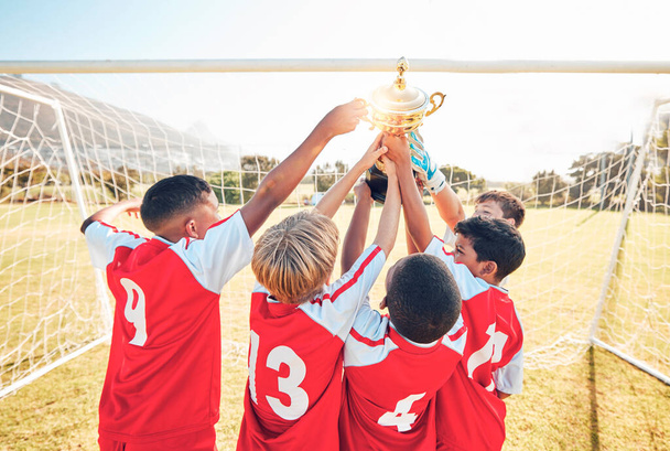 Children, winner and team soccer with trophy celebrating victory, achievement or match on the field. Kids in celebration for teamwork, sports and football match or game win together in the outdoors. - 写真・画像