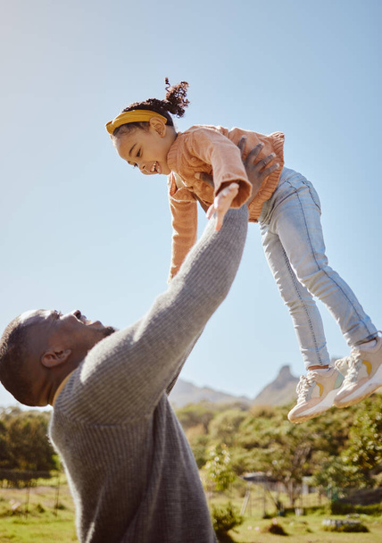 Vader tilt kind in de lucht op park, tuin en natuur buiten voor plezier, hechting en kwaliteit tijd samen als zwarte familie. Papa gooien meisje kind in de lucht tijdens het spelen met liefde, zorg en ontspanning. - Foto, afbeelding