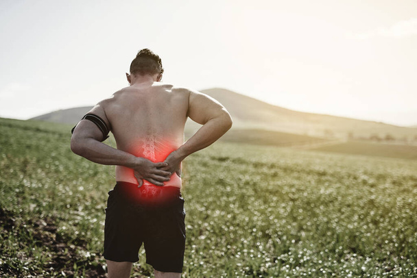 Hes got some serious back pain. Rearview shot of a young man exercising with an injury highlighted by cgi - Photo, Image