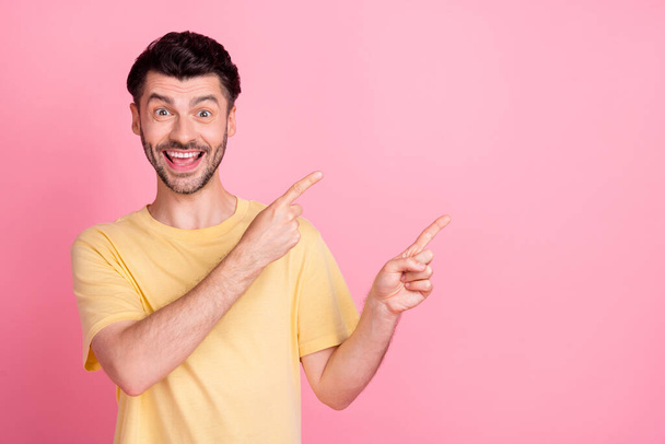 Photo of funny good mood guy with brunet hair dressed yellow t-shirt indicating empty space sale isolated on pink color background. - Fotoğraf, Görsel