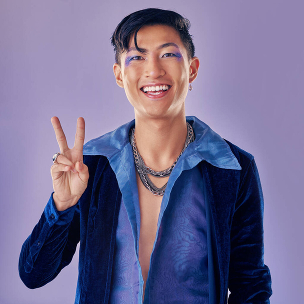 Fashion, peace sign and smile of punk man in studio with smile and vintage, retro or pop art clothes on color background for motivation. Gen z asian aesthetic lgbt or gay model with pride on purple. - Photo, Image