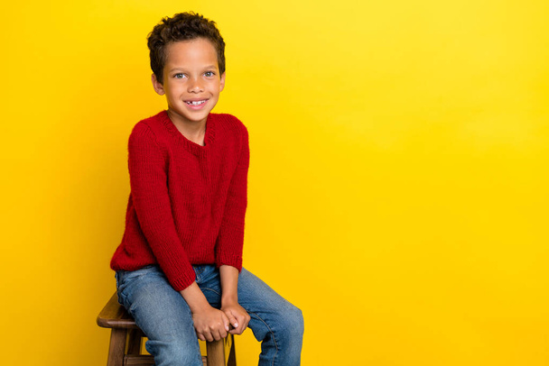 Photo portrait of charming small boy sit chair interview relax rest dressed stylish red knitted look isolated on yellow color background. - Fotografie, Obrázek