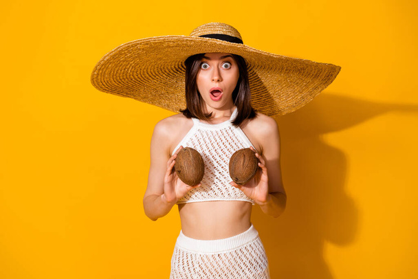 Photo of impressed shocked girl dressed knitted bra straw cap holding coconut boobs isolated yellow color background. - Foto, Imagem