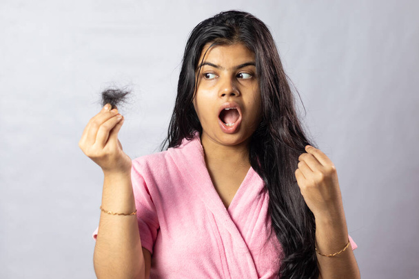 Una ragazza indiana preoccupata in accappatoio rosa con problemi di caduta dei capelli su sfondo bianco - Foto, immagini