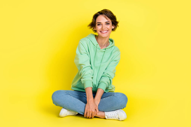 Full length photo of adorable sweet girl dressed green sweatshirt sitting legs crossed isolated yellow color background. - Фото, изображение