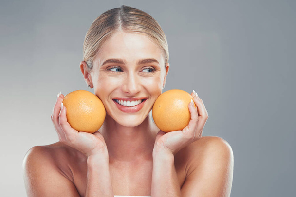 Orange, skincare and woman thinking of cosmetics, beauty and health of body against a grey mockup studio background. Happy, healthy and young model with vitamin c fruit for wellness and diet. - Photo, Image