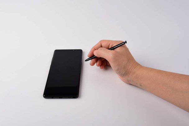Pen in de hand en smartphone en zwarte stylus voor het schrijven geïsoleerd op witte achtergrond.  - Foto, afbeelding