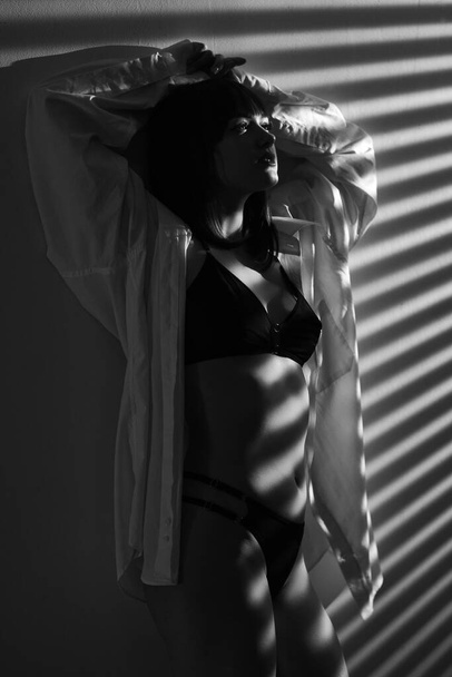 Femme brune sexy avec un corps mince parfait debout près du mur. Portant une lingerie noire élégante et une chemise blanche pour petit ami. Espace de copie - Photo, image