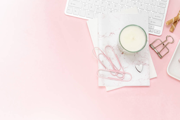 A feminine woman workspace, with a silver keyboard of a computer on a pastel pink background with copy space. Banner image with candle and other office space and desktop white stationery - Foto, imagen