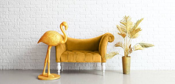 Goldener Flamingo, bequemer Sessel und Vase mit Palmblättern in der Nähe der weißen Ziegelwand im Zimmer - Foto, Bild