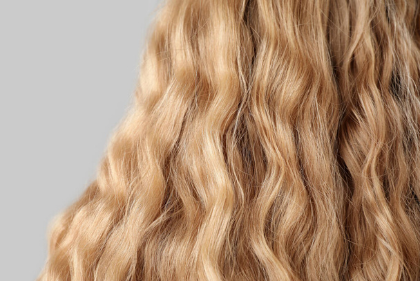Close-up uitzicht van krullend blond haar op lichte achtergrond - Foto, afbeelding