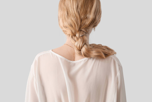 Blonde woman in blouse with pigtail hairstyle on light background - Фото, зображення