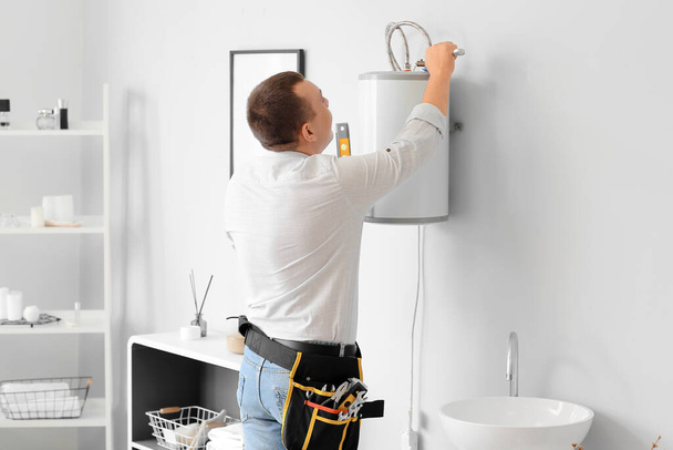 Male plumber repairing electric boiler with wrench in bathroom - Foto, Imagen