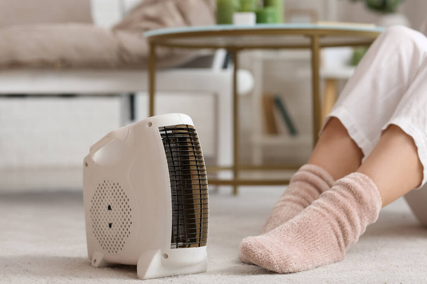Modern electric fan heater and woman in warm socks on carpet, closeup - Fotó, kép