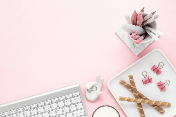 Egy nőies női munkaterület, egy ezüst billentyűzetű számítógéppel, pasztell rózsaszín háttérrel, fénymásoló felülettel. Bannerkép gyertyával és más irodahelyiséggel és asztali fehér írószerrel - Fotó, kép