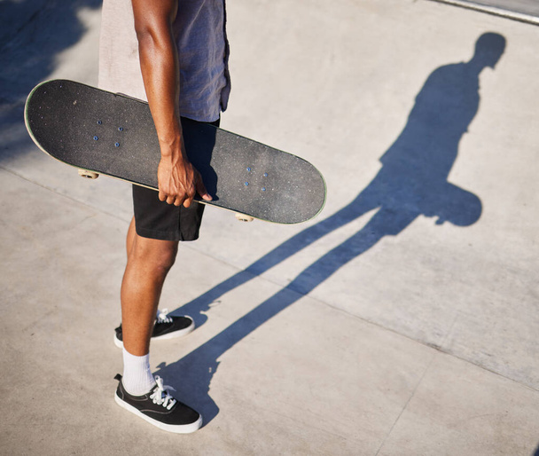 Kaykay, spor ve elinde eğlence için sörf tahtası tutan bir adam, parkta ata biniyor ve oynuyor. Bacaklar, gölge ve havalı kaykaycı ya da kaykaylı şehir sporu ve stili için kaykay yapan. - Fotoğraf, Görsel
