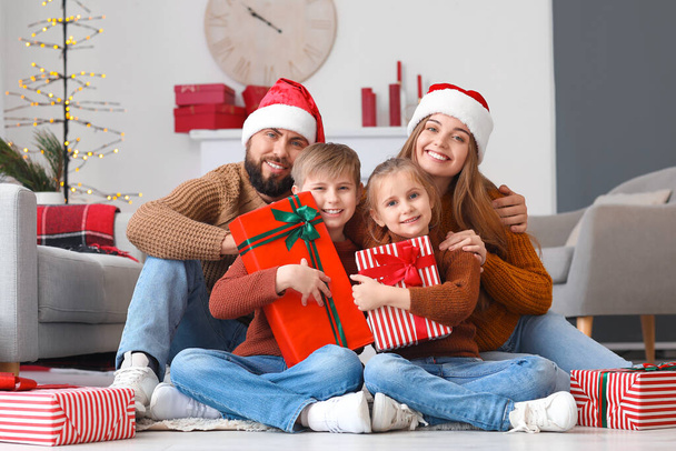 Ευτυχισμένοι γονείς με καπέλα και τα μικρά παιδιά τους με χριστουγεννιάτικα δώρα στο σπίτι - Φωτογραφία, εικόνα