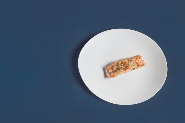 An overhead view of a serving of a lemon salmon loin with parsley and garlic on a white plate and textured blue studio background. Fish and food. - Foto, afbeelding
