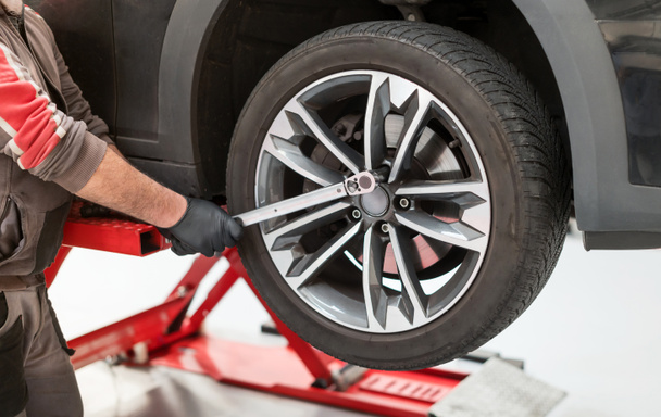 Erntehelfer in Uniform mit Drehmomentschlüssel, um Reifen vom Auto auf Hydraulikheber während der Arbeit in der Garage zu entfernen - Foto, Bild