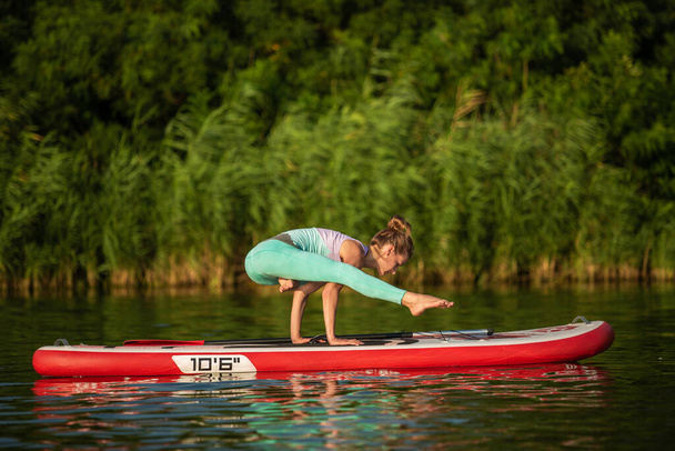 Молодая женщина занимается йогой на гребной доске SUP на красивом озере или реке. Концепция здорового образа жизни. Спорт. Йога. Хобби
 - Фото, изображение