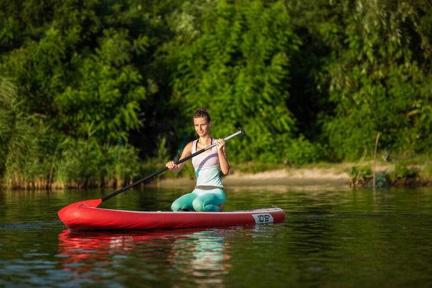 Young athletic woman doing fitness on a board with an oar on a lake. The concept of a healthy lifestyle. Sport. Yoga. Hobby - Foto, Bild