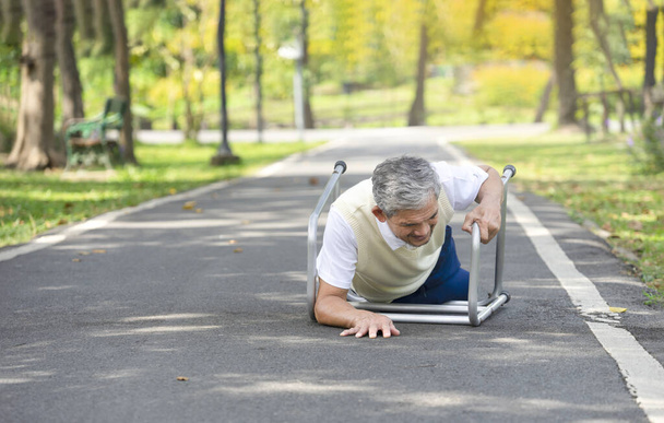 senior man viel op zijn looprek tijdens het wandelen in het park, concept ouderen vallen, medische zorg, risicobeheer van de herfst - Foto, afbeelding