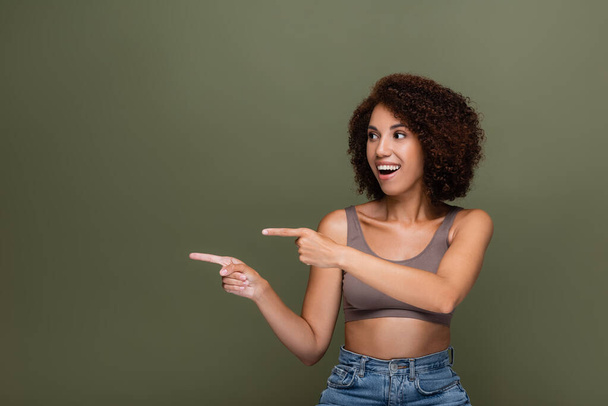 Smiling african american woman pointing with fingers isolated on green  - Photo, image
