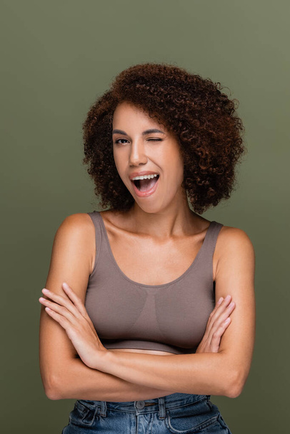 Young african american woman in top winking at camera isolated on green  - Photo, image